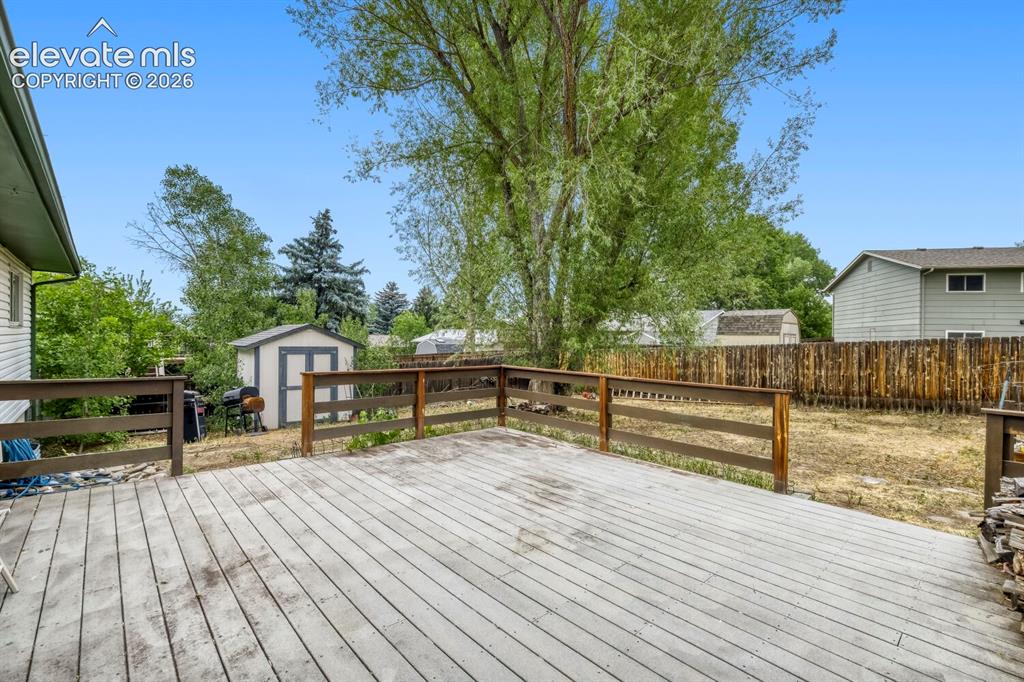 Image 24 of 26: Spacious outdoor deck with wood railing, featuring a large backyard, mature