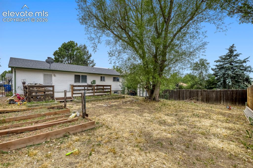 Image 25 of 26: Expansive backyard with a large mature tree, wood fencing, and raised garde