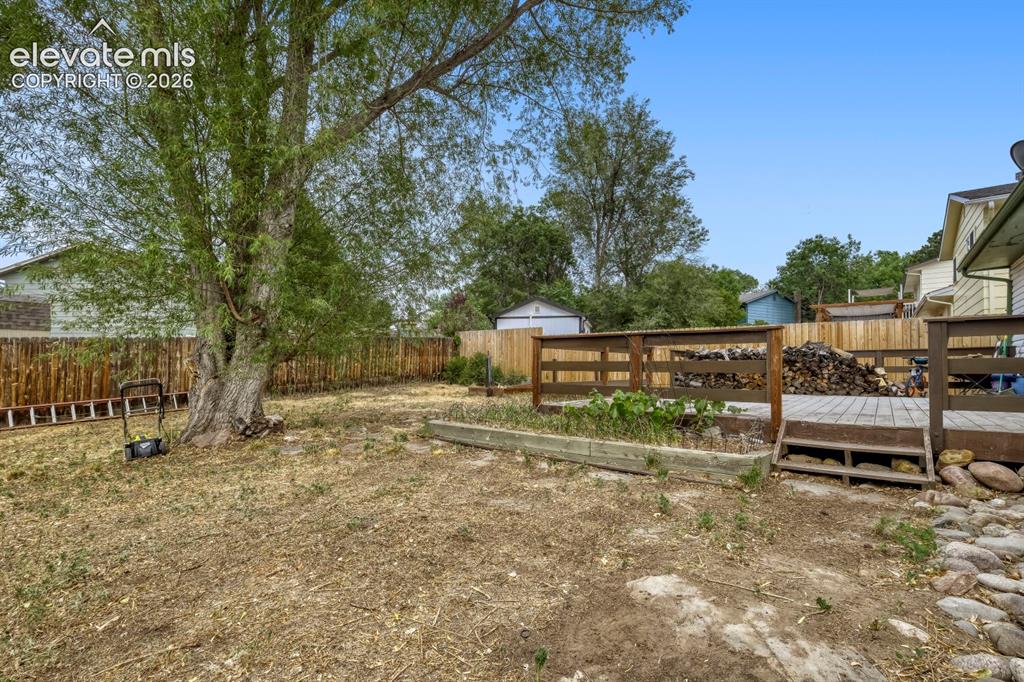 Image 26 of 26: Spacious backyard featuring a large tree, wooden fencing, a raised garden b