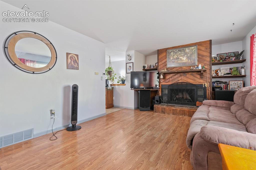 Image 4 of 26: Living area featuring wood-finish flooring, a fireplace with a wood surroun
