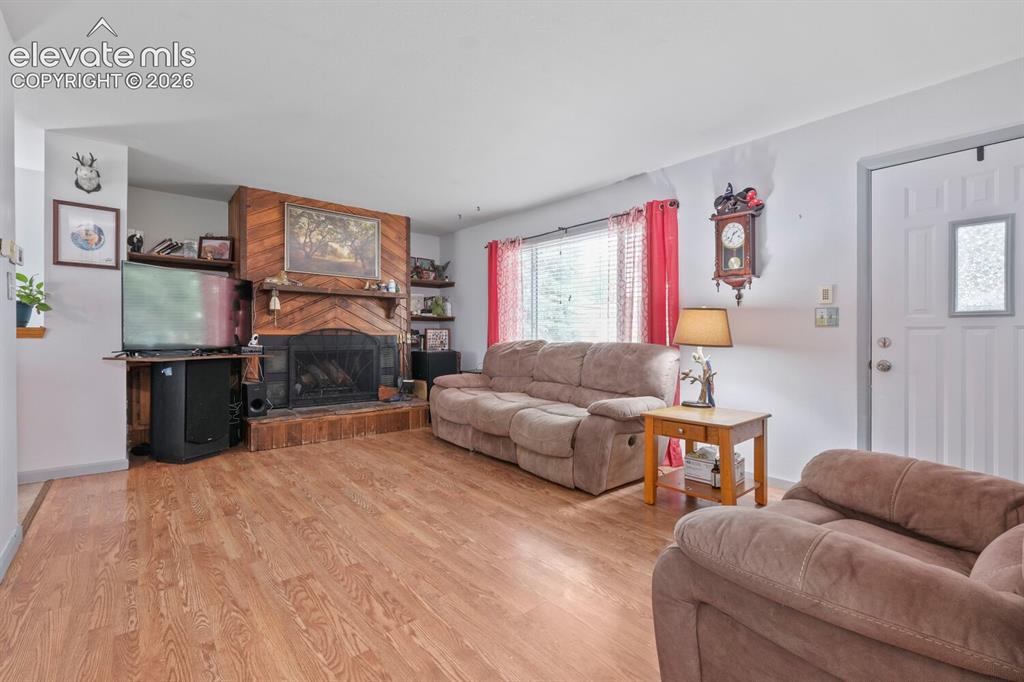 Image 5 of 26: Spacious living area featuring wood-finish flooring, a prominent fireplace