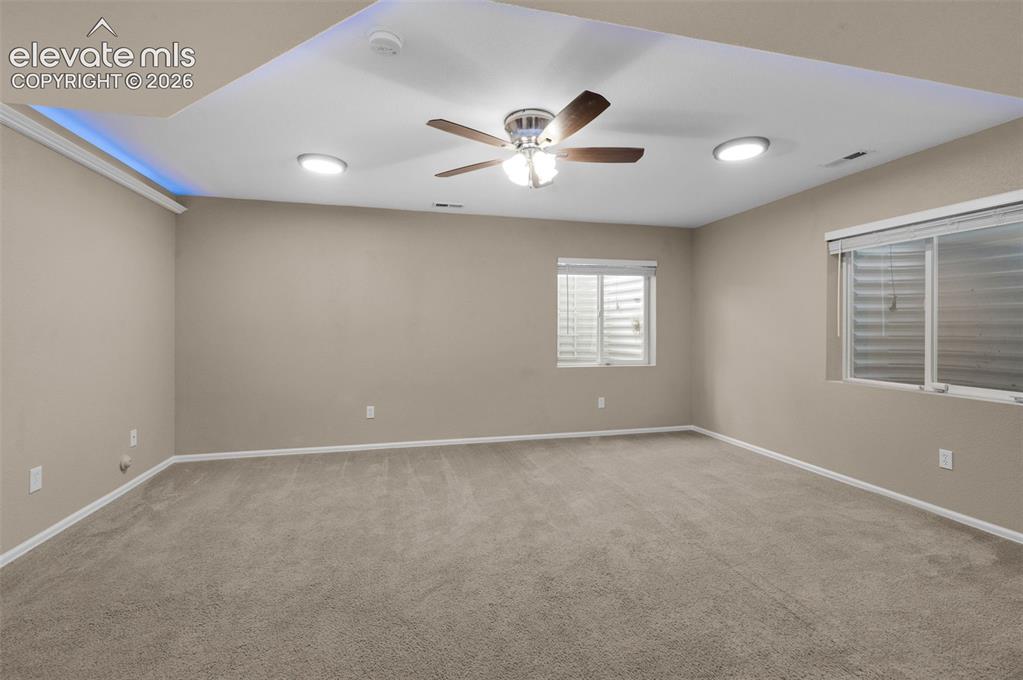 Image 10 of 41: Large finished basement media room with distinctive tray-ceiling lighting.