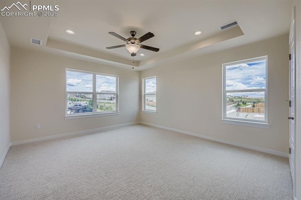 Image 12 of 28: Unfurnished room with a raised ceiling, a ceiling fan, light colored carpet