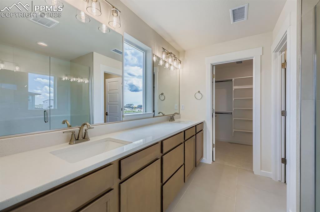 Image 15 of 28: Bathroom featuring a stall shower, double vanity, a spacious closet, and ti