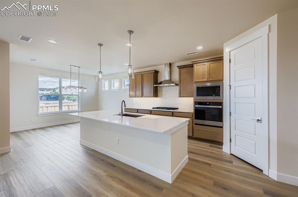 Image 7 of 28: Kitchen with stainless steel appliances, wall chimney range hood, light woo