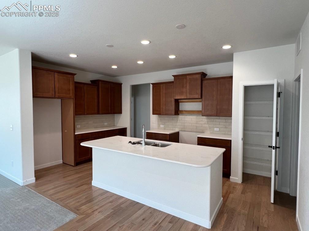 Image 3 of 7: Kitchen with light wood finished floors, decorative backsplash, an island w