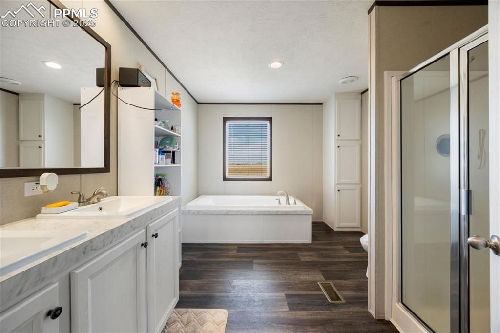 Image 9 of 40: Bathroom with dark wood finished floors, a shower stall, double vanity, a b