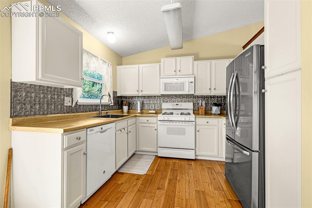 Image 10 of 37: Kitchen featuring white appliances, backsplash, light wood-style floors, a