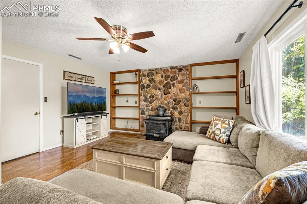 Image 15 of 37: Living area with a wood stove, wood finished floors, a textured ceiling, an
