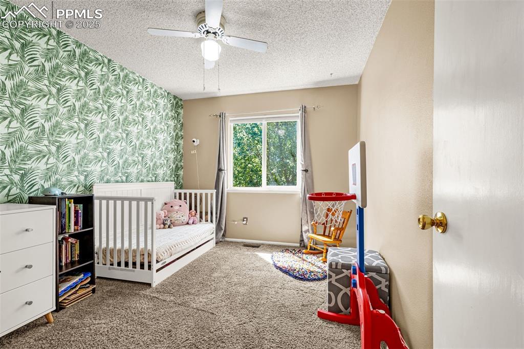 Image 18 of 37: Bedroom with carpet, wallpapered walls, a nursery area, ceiling fan, and a