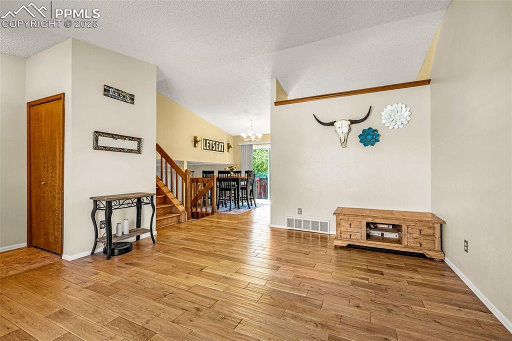 Image 5 of 37: Living room with a chandelier, a textured ceiling, stairway, light wood-sty