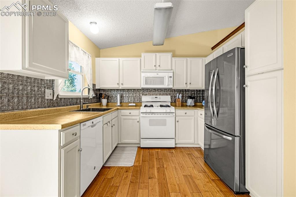 Image 9 of 37: Kitchen featuring white appliances, backsplash, light wood-style flooring,