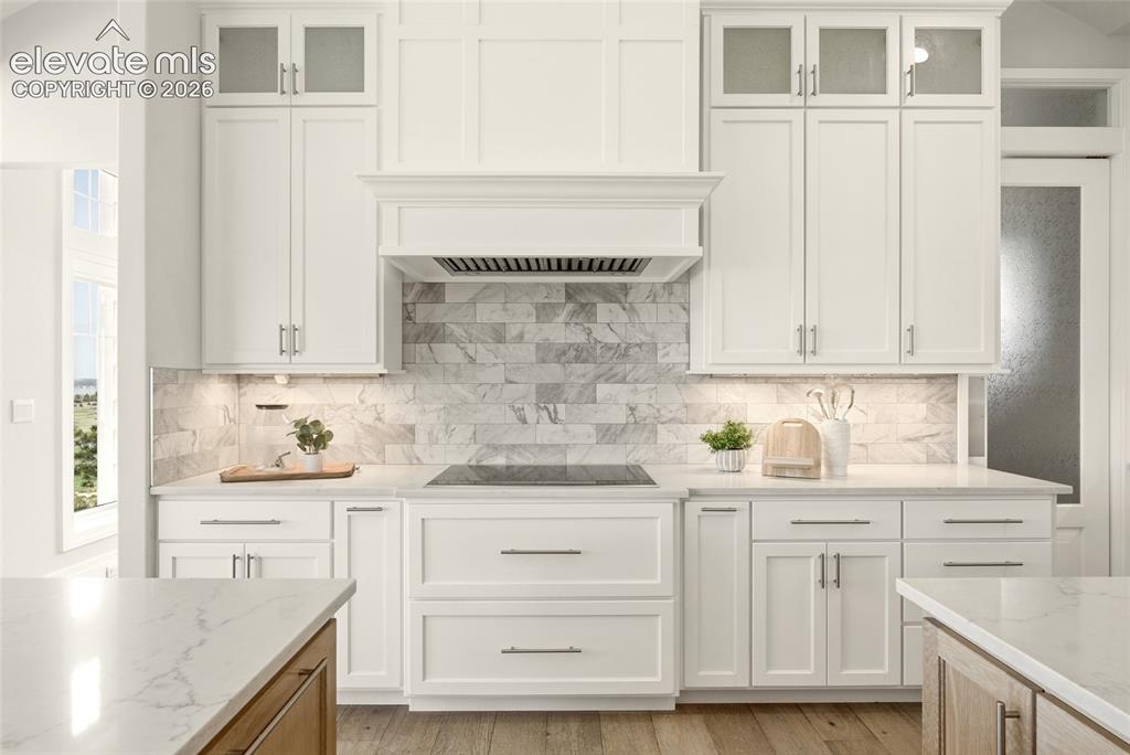 Image 10 of 50: Kitchen featuring white shaker-style cabinetry, a built-in range hood, ston