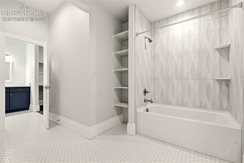 Image 32 of 50: Bathroom featuring a built-in tub with a shower fixture, textured white til