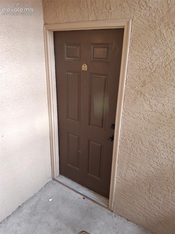 Image 1 of 10: Paneled entry door with contrasting trim and textured exterior walls