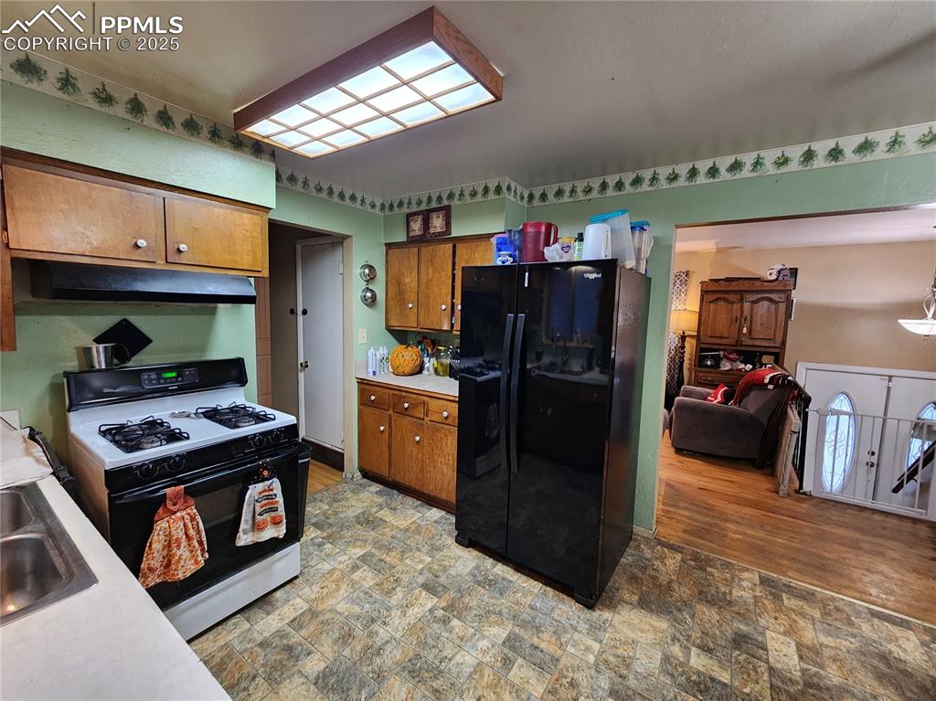 Image 9 of 33: Kitchen with gas range, black refrigerator, brown cabinets, light counterto
