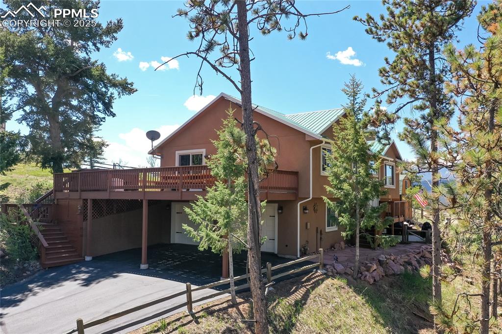 Image 2 of 44: Side of house with a wooden deck, stucco siding, stairway, and metal roof