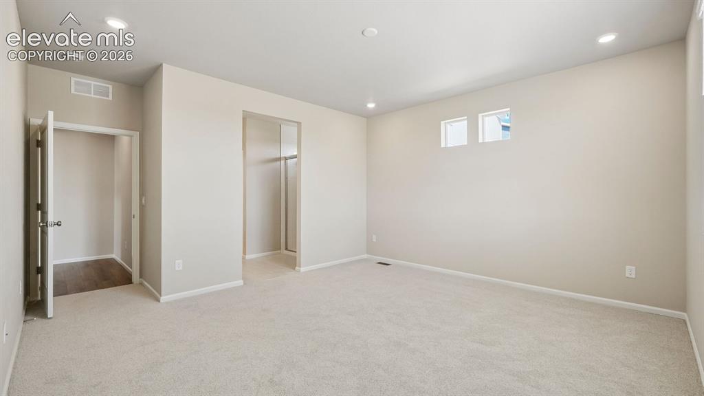 Image 28 of 47: Recessed lighting and two high-set windows illuminate this carpeted room