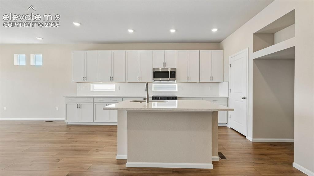 Image 8 of 47: Kitchen featuring a central island with an undermount sink, white cabinetry