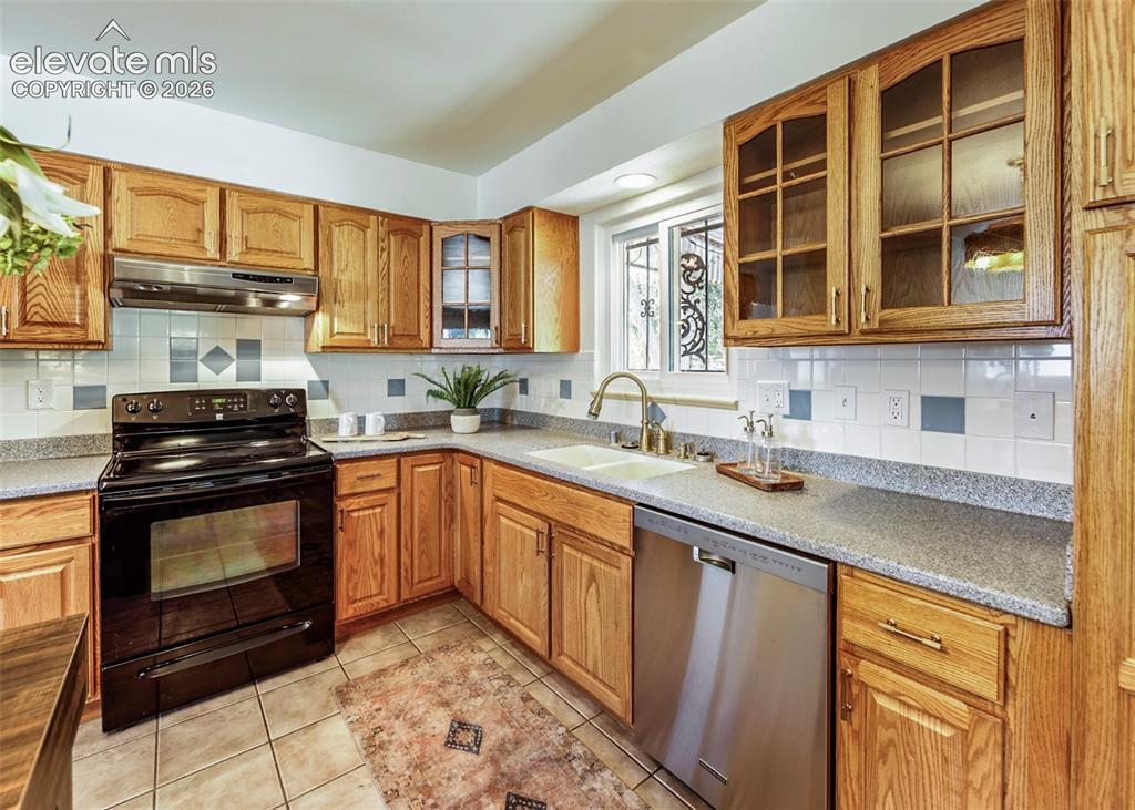 Image 19 of 48: Wood cabinetry, stainless steel dishwasher, black oven range, tile backspla