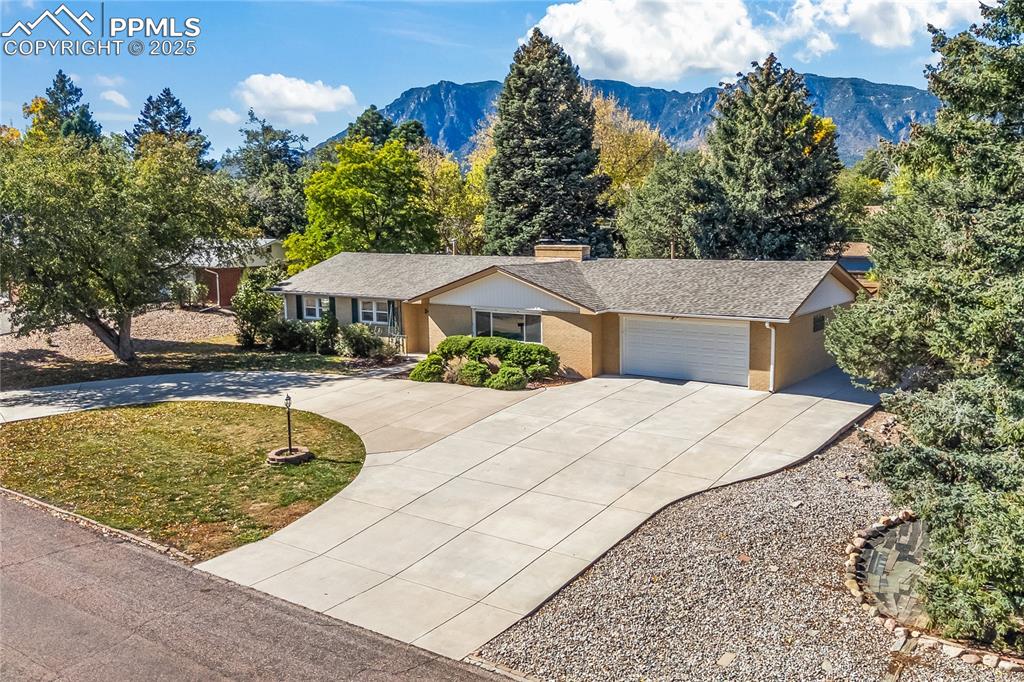 Caption: Ranch-style house with concrete driveway, a chimney, a mountain view, a front yard, and an attached 