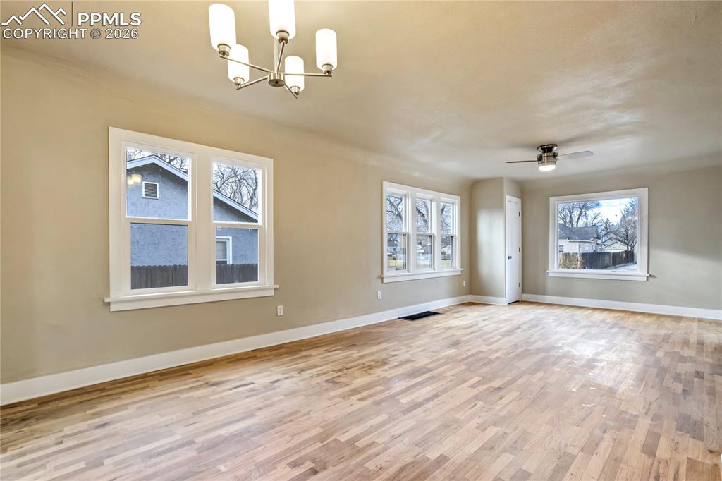 Image 4 of 28: Bright living room with wood floors, ceiling fan, chandelier, and abundant 