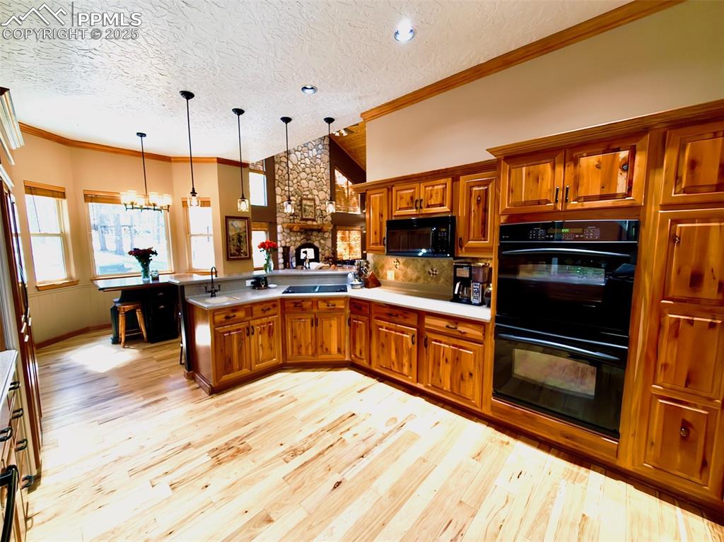 Image 10 of 50: Kitchen featuring brown cabinetry, crown molding, tasteful backsplash, blac