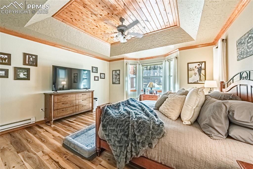 Image 15 of 50: Bedroom with a tray ceiling, wood finished floors, ornamental molding, base