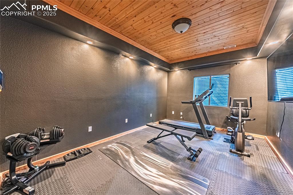 Image 44 of 50: Workout area with a textured wall, wood ceiling, and ornamental molding
