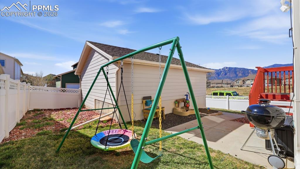 Image 41 of 50: Fenced backyard with concrete patio and grass area with play set that stays