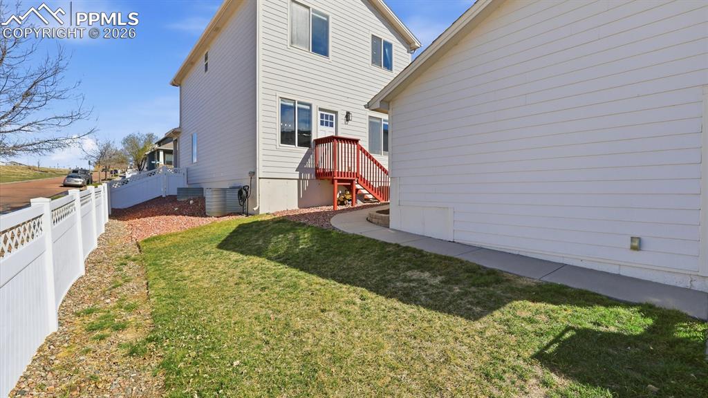 Image 43 of 50: Fenced backyard with concrete patio and grass area with play set that stays