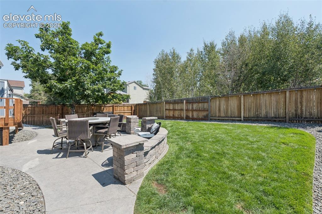 Image 20 of 31: Expansive lawn area with a perimeter wood fence, large concrete patio, and