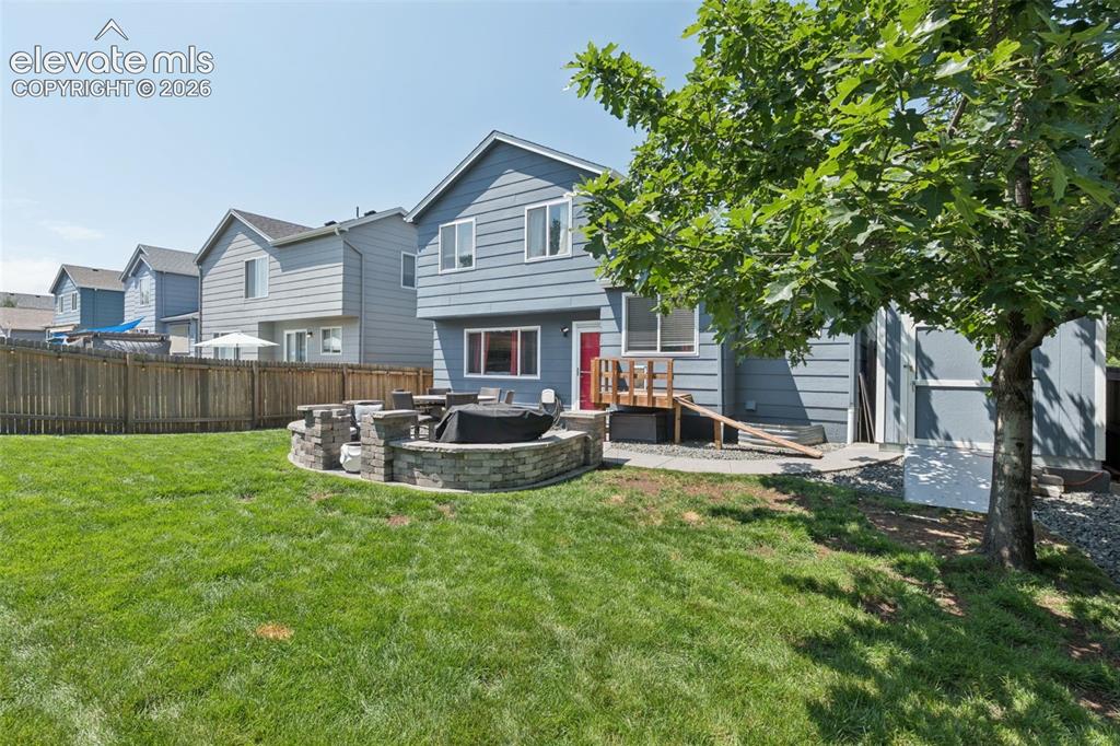 Image 22 of 31: Expansive backyard featuring a stone-clad fire pit, concrete patio, privacy