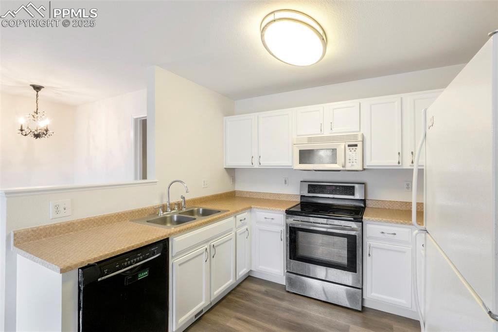Image 12 of 31: Kitchen with white appliances, white cabinetry, light countertops, dark woo