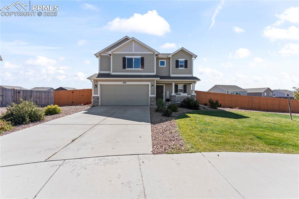 Caption: View of front of home with concrete driveway, stone siding, an attached garage, and a porch