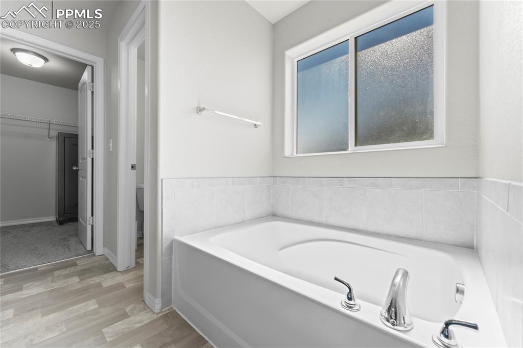 Image 13 of 40: Bathroom featuring a bath, a spacious closet, and light wood-style floors
