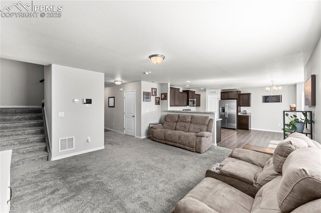 Image 18 of 40: Living area featuring stairway, a chandelier, and light carpet