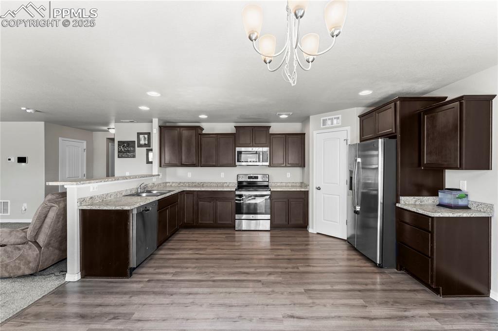 Image 21 of 40: Kitchen featuring dark brown cabinetry, stainless steel appliances, dark wo