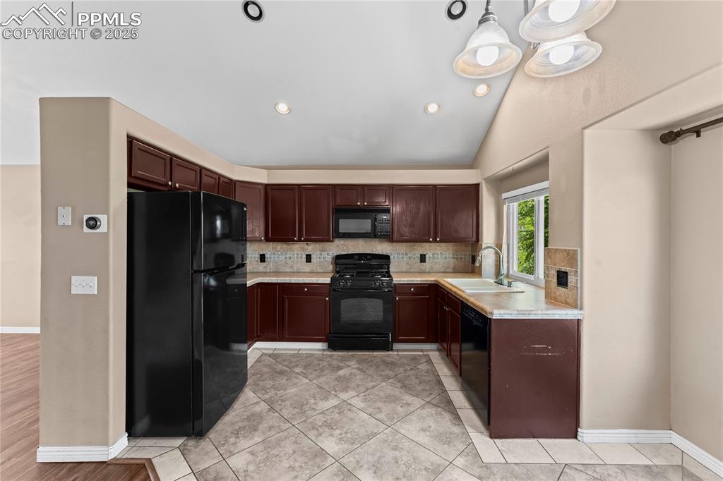 Image 10 of 42: Kitchen with backsplash, black appliances, light countertops, vaulted ceili