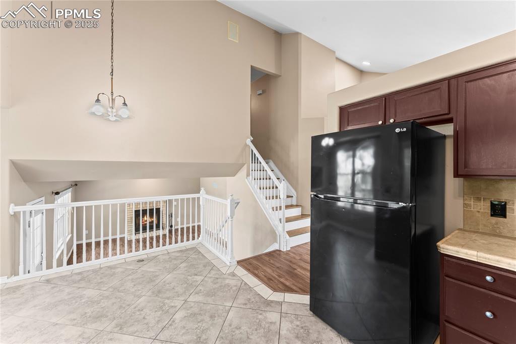 Image 12 of 42: Kitchen featuring freestanding refrigerator, a lit fireplace, light tile pa