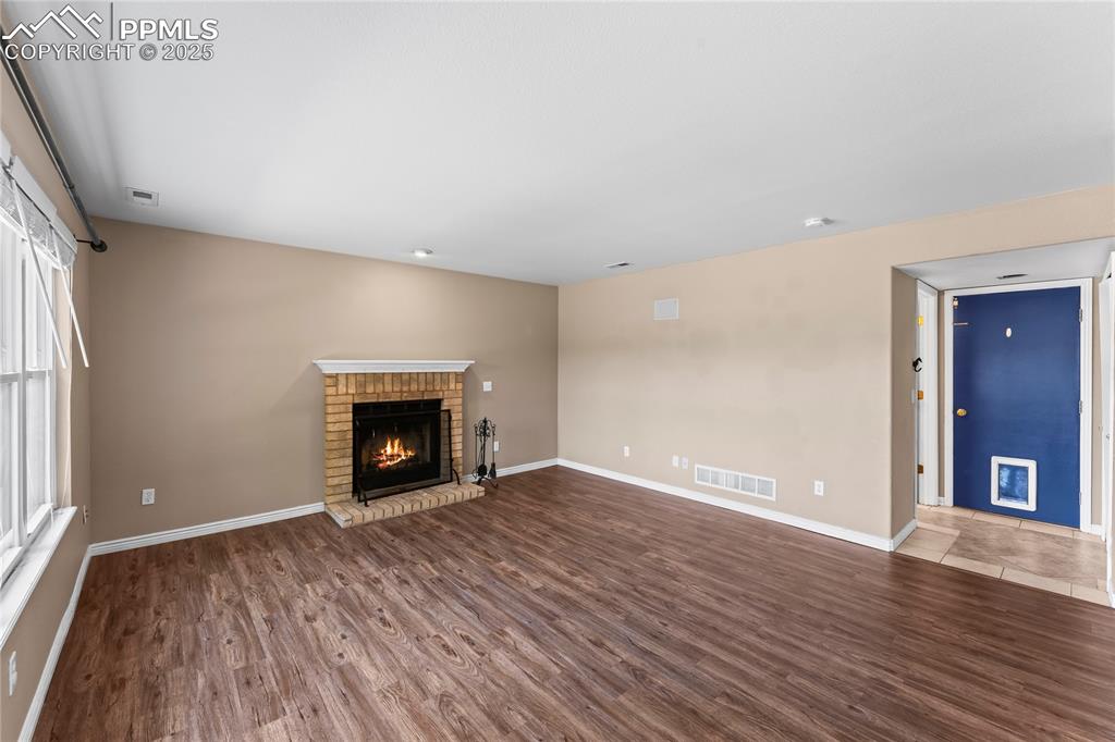 Image 16 of 42: Unfurnished living room featuring a brick fireplace and wood finished floor