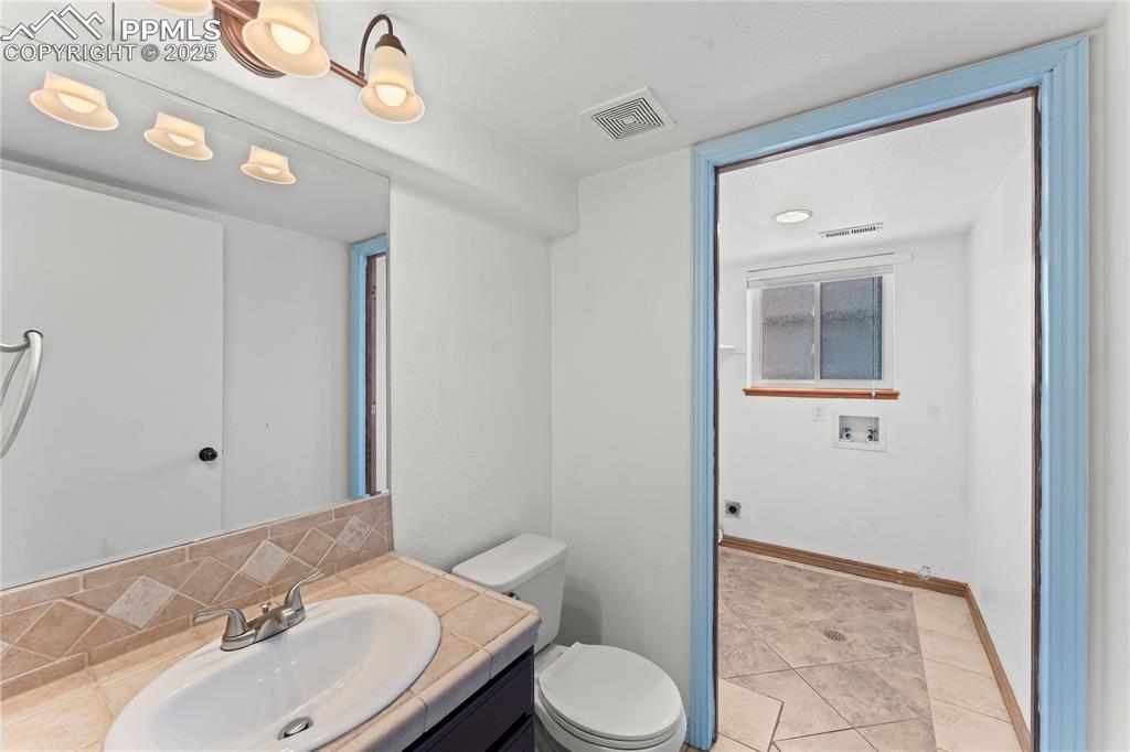 Image 18 of 42: Half bath with tile patterned flooring, vanity, and tasteful backsplash