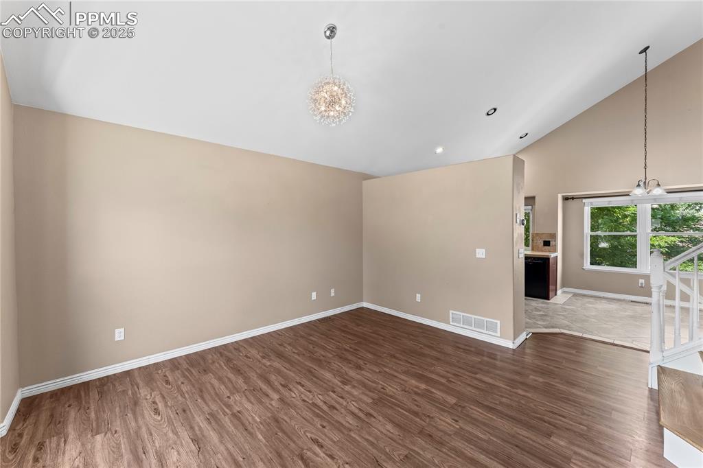 Image 5 of 42: Spare room with a chandelier, wood finished floors, high vaulted ceiling, a