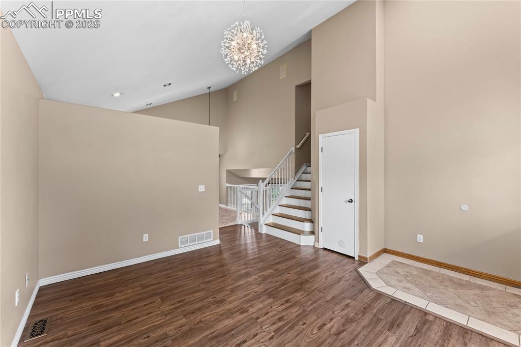 Image 6 of 42: Unfurnished room featuring wood finished floors, stairway, high vaulted cei