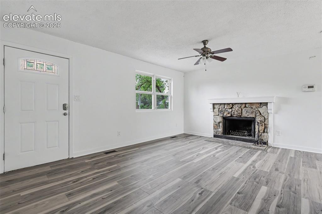 Image 12 of 43: Spacious living area featuring wood-finish flooring, a stone fireplace with