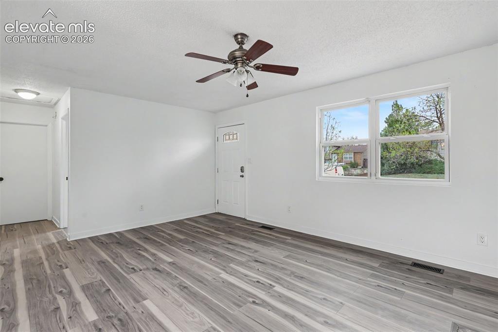 Image 14 of 43: Spacious living area featuring wood-finish flooring, white walls, and a cei