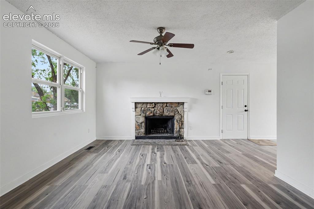 Image 19 of 43: Spacious room featuring wood-finish flooring, a stone fireplace with a whit
