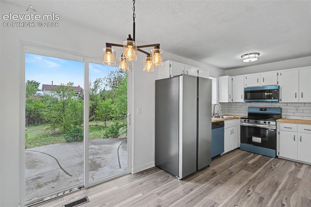 Image 22 of 43: Kitchen with wood-finish flooring, white cabinetry, and light wood-tone cou