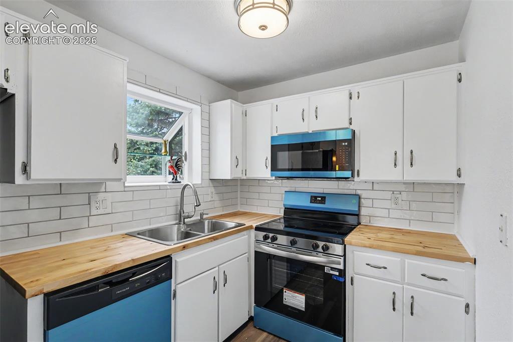 Image 24 of 43: Kitchen featuring white cabinetry, wood-finish countertops, a subway tile b