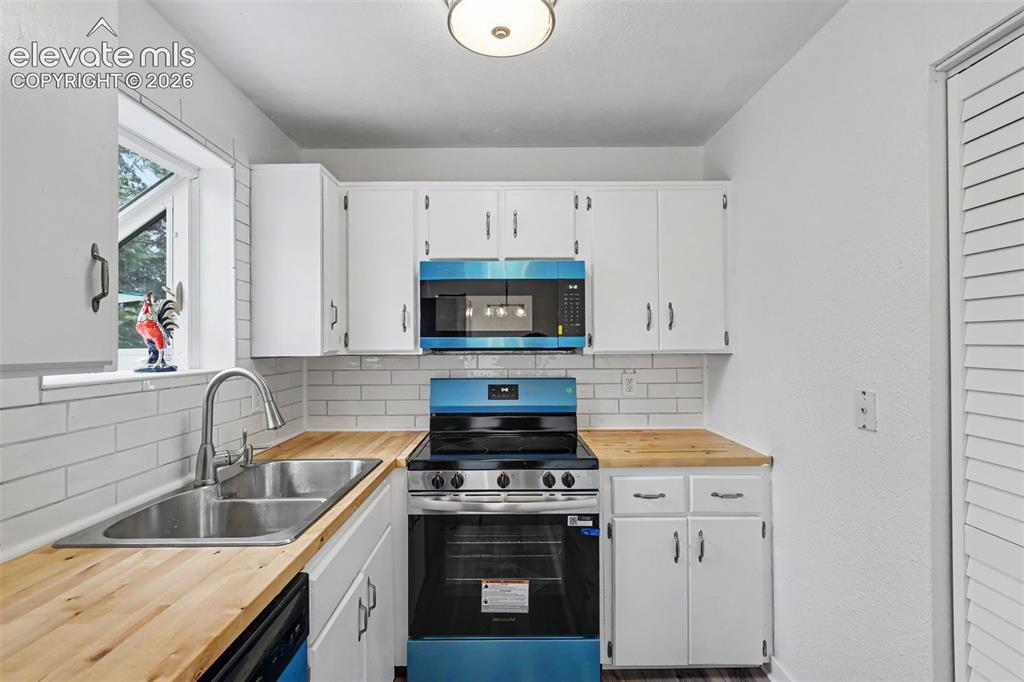 Image 25 of 43: Kitchen featuring white cabinetry, wood-finish countertops, subway tile bac